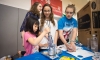 Joyce Chan, left, a 3rd-grader at New Haven Elementary (Boone County), presses an image into a button with the help of Audrey Wilson and Tessa Hutchinson, both 8th-graders at Gray Middle School (Boone County) during the World Maker and Inventor Expo at Boone County High School. Photo by Bobby Ellis, April 23, 2016