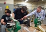 Nick Stinson, left, gets help from carpentry instructor Will Farmer and former principal Tom Thompson as he cuts out letters for the wooden version of the logo. Photo by Bobby Ellis, Dec. 21, 2016