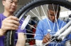 Volunteer Fang Ping holds the wheel steady as 7th-grade student Elijah Crosby tightens the bolts. Crosby said being in the club has boosted his courage and confidence. Photo by Amy Wallot, April 13, 2015