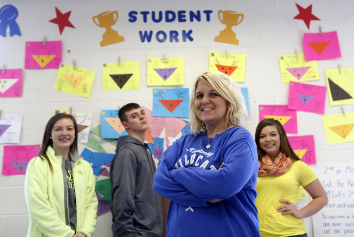 Teachers at East Carter High School (Carter County) are to post student proficient work, learning targets and class mission statements in their rooms. Geometry teacher Amanda McCall, pictured with sophomores Kristen Mayo, Chaseton Tussey and Joscelyn Wilcox, in front of her student work wall. Photo by Amy Wallot, Dec. 12, 2014