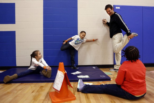 Tates Creek Elementary School (Fayette County) P.E. teacher Daniel Hill demonstrates stretching before running to 1st-grade students Camryn Mullins, MyKel Allen and Mikaila Mason. The class was learning about locomotor skills and was broke down into different center including running, jumping, leaping and skipping. Photo by Amy Wallot, Feb. 2, 2015