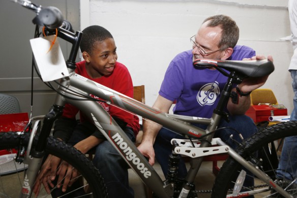 Jayshaun Washington and Doug Dicken, a volunteer from GE, joke around as they assemble a bike during the STEM Bike Club at Holmes Middle School (Covington Independent) bike club. Photo by Amy Wallot, April 13, 2015