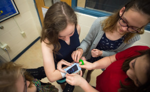 Hailey Poe, from left, Hannah Sipple, Janie Pierce and Lauren Freeman try to secure a device onto the arm of fellow Sipple. The device helps secure an iPhone to the user’s wrist. Photo by Bobby Ellis, April 7, 2016