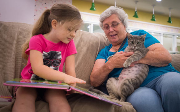 Addlyn Adkins, left, and her grandmother Juanita Adkins read to a cat at the Kyova Mall in Ashland. Photo by Bobby Ellis, July 12, 2016