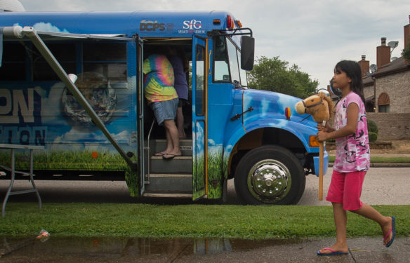 Cing de Lun, a student at Southern Oaks Elementary School (Daviess County) rides a stick horse past the Exploration Station bus during its weekly stop in a neighborhood that is home to part of the Owensboro area’s growing refugee population. The bus was introduced this year as a mobile educational center to help schools in the district combat summer slide. Photo by Bobby Ellis, July 18, 2016