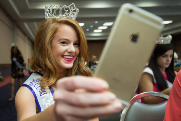 Owen County Fair Queen Veronica Chisolm takes a selfie after adjusting her crown during the Junior Mister and Miss State Fair Pageant. County fair pageant winners are given scholarships to different universities depending on what place they come in during their respective pageants and many work to support different charities during their time holding the crown. Photo by Bobby Ellis, Aug. 18, 2016