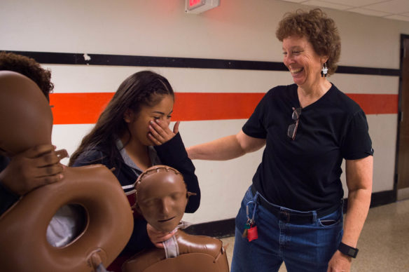 Diane Polley, a health and P.E. teacher at Fern Creek High School (Jefferson County), helps students carry CPR practice dummies to the gym. Seth Jones, left, a student at Fern Creek High School (Jefferson County), Kenza Magouh and Megan Schilling practice CPR on dummies during a hands-only CPR class. Photo by Bobby Ellis, Sept. 23, 2016