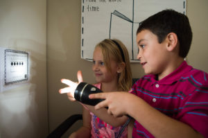 Olivia Wells, left, and Micah Tanner use a flashlight to cast shadows on a wall during an experiment in Kara Northern's first-grade class. Photo by Bobby Ellis, Oct. 17, 2016