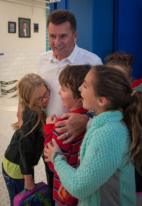 Bob Blankenship, a retired principal at Poage Elementary School (Ashland Independent), is hugged by students as he enters the gym to watch a noonball game. Blankenship created noonball in 1995 as a recess activity that all students could take part in during the winter months. Photo by Bobby Ellis, Nov. 29, 2016