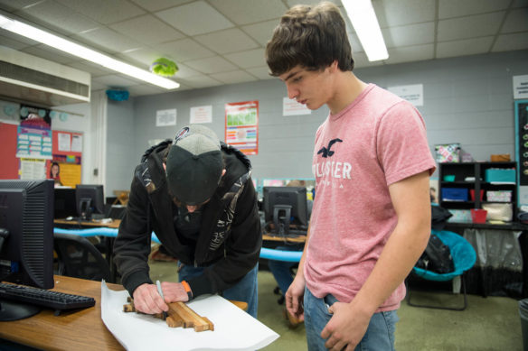 Bennett Sosbe, left, and Hunter Gaunce, sophomores at Harrison County Area Technology Center, trace a cutting board that they plan to make as part of a business they started in Amber Florence's entrepreneurship class. Students in the class have started their own enterprises to sell goods and services. Photo by Bobby Ellis, Dec. 5, 2017