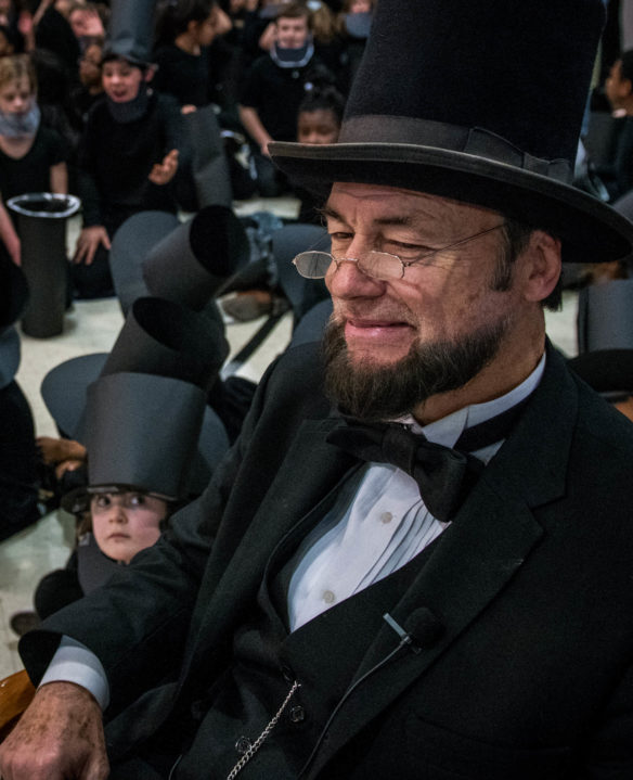 Larry Elliott, an Abraham Lincoln living history actor, watches as students enter the Lincoln Elementary Performing Arts School gym. Photo by Bobby Ellis, Feb. 14, 2018