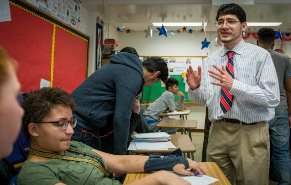 Chris Woo, right, a teacher at Seneca High School (Jefferson County), talks to Courtney Newton, left, during Woo's AP Government and Politics class. Paying for AP exams for qualifying students could improve those students' chances for success in college and removes a financial obligation for districts. Photo by Bobby Ellis, March 19, 2018