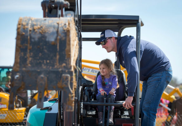 Haly Brown is shown how to drive an excavator by Andrew Arlinghouse during the Big Dig, an event at the Boone County Fair grounds meant to introduce children to the building and construction industry. Photo by Bobby Ellis, April 21, 2018