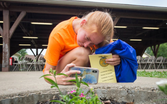 Brooke Lanhal, a student at Apollo High School (Daviess County), uses her phone to take a picture of a flower as part of her photography homework for her FFA Advocacy class at the FFA summer camp. Photo by Bobby Ellis, June 12, 2018