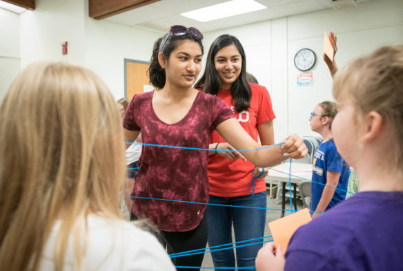 Arushi Gupta, left, and Janjana Kothari hand out yarn as STEM You Can! goers make a food web in a game where they decide whether a certain organism is either a producer or consumer. Photo by Bobby Ellis, June 13, 2018