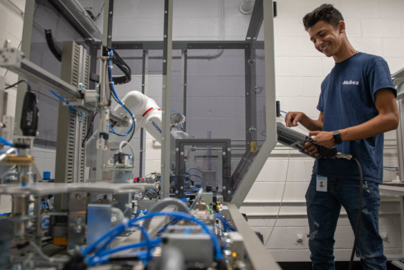 Michah Schenck programs a production simulator used to train apprentices at Mubea Inc. on troubleshooting the company's manufacturing robots. Schenck has entered the company’s apprenticeship program, which will take about 3 1/2 years to complete. Photo by Bobby Ellis, July 18, 2018