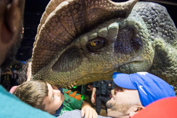 Ryan Shive, left, and Jase Ford are nusseled by a dinosaur during the "Meet a Dinosaur" encounter at Jurassic Quest. Photo by Bobby Ellis, July 6, 2018