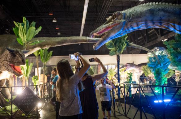 Jurassic Quest goers take pictures of animatronic dinosaurs as they walk through a replica of an a prehistoric jungle in Rupp Arena. Photo by Bobby Ellis, July 6, 2018