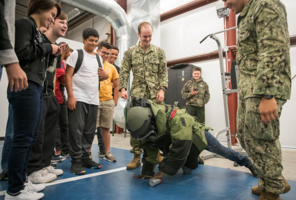 Abdullahi Otun attempts to grab a can off the floor while wearing a bomb suit. Photo by Bobby Ellis, Aug. 23, 2018