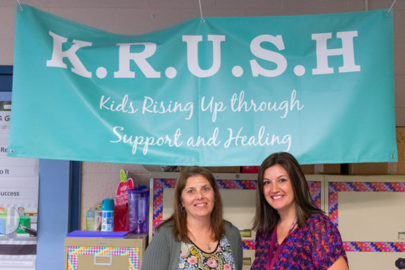 Kristi Whittaker, left, and Jalina Wheeler stand in front of a sign for the Kids Rising Up through Support and Healing (KRUSH) program.