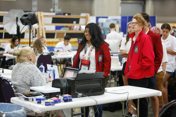 Chosalin Morales, center, a student a Newport High School (Newport Independent) competing in photography at the SkillsUSA Championships, turns in a flash drive containing her photos. Photo by Mike Marsee, June 26, 2019