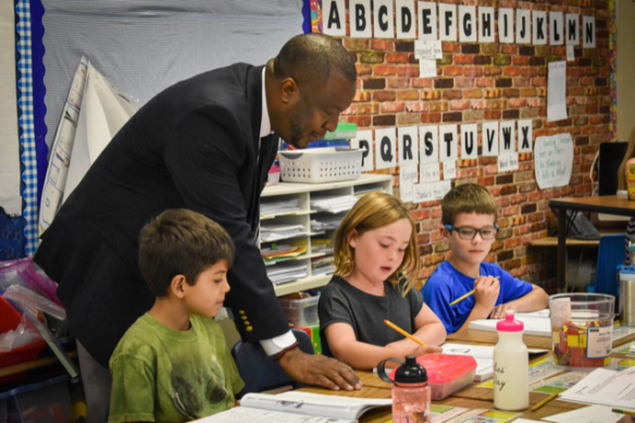 Thomas Woods-Tucker leans over a table with three young students as one of them describes what she is working on.