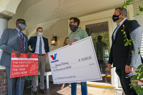 Donnie Piercey on his porch holding a large check for $10,000 with state and local education officials.