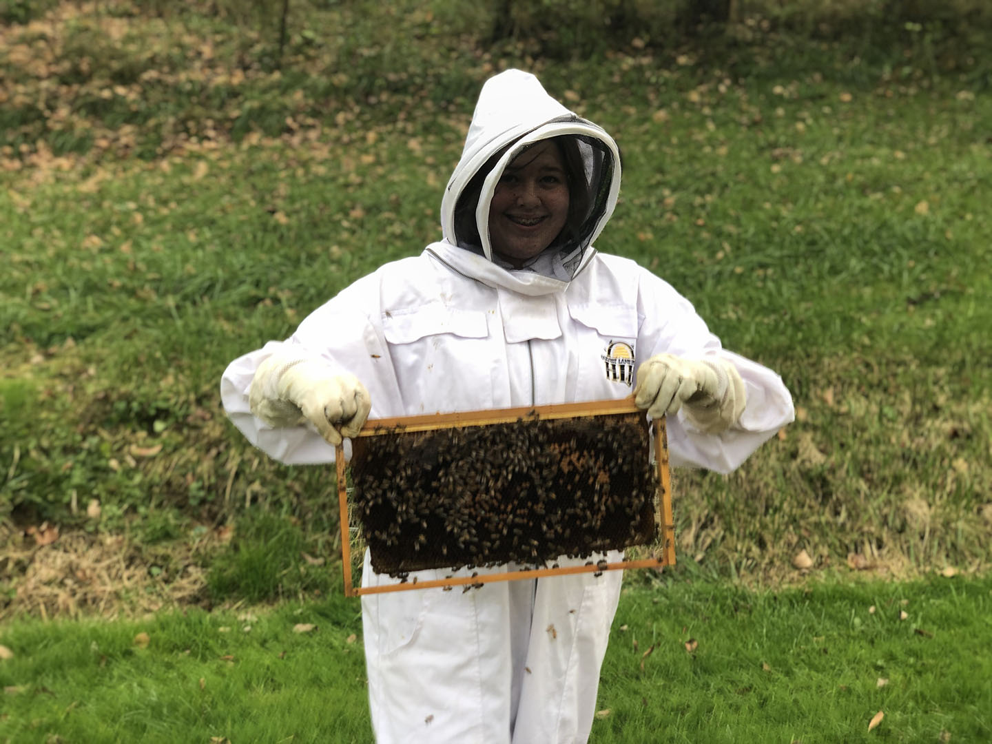 Picture of Emma Stevens wearing a beekeepers outfit and holding a rack from her hive filled with bees.
