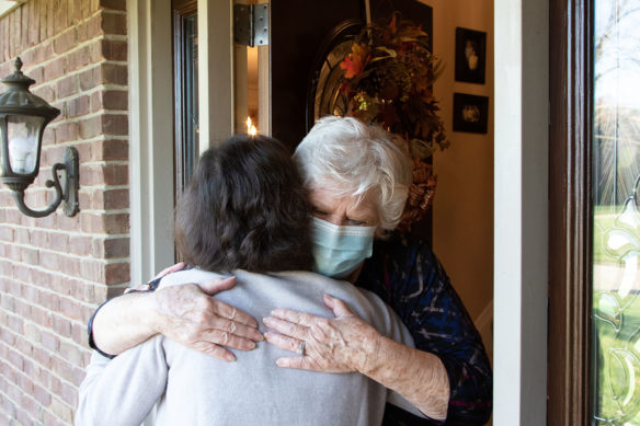 Two women hug at the front door of a brick house.