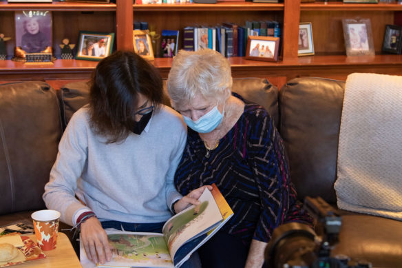 Two women sit on a couch looking through a picture book.