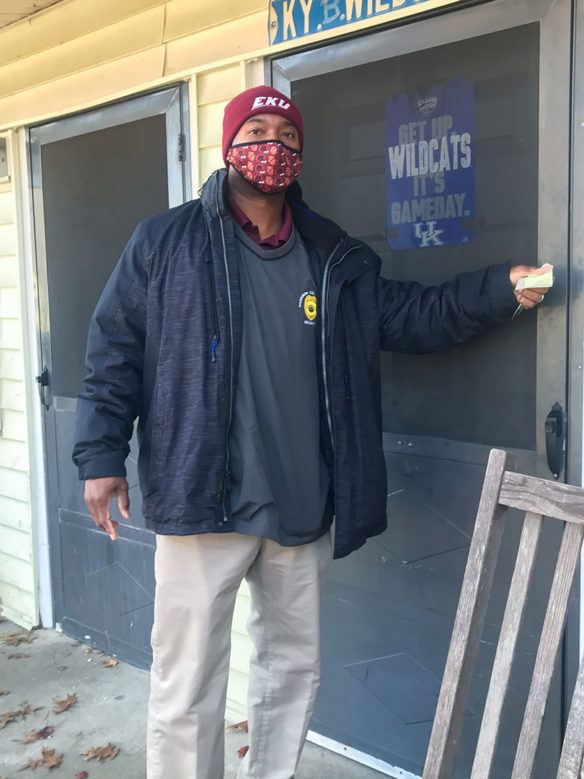 A man wearing a face covering knocks on the front door of a house.