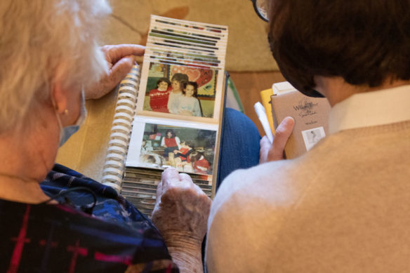 A photo from over the shoulder of two women sitting on a couch and looking at pictures.