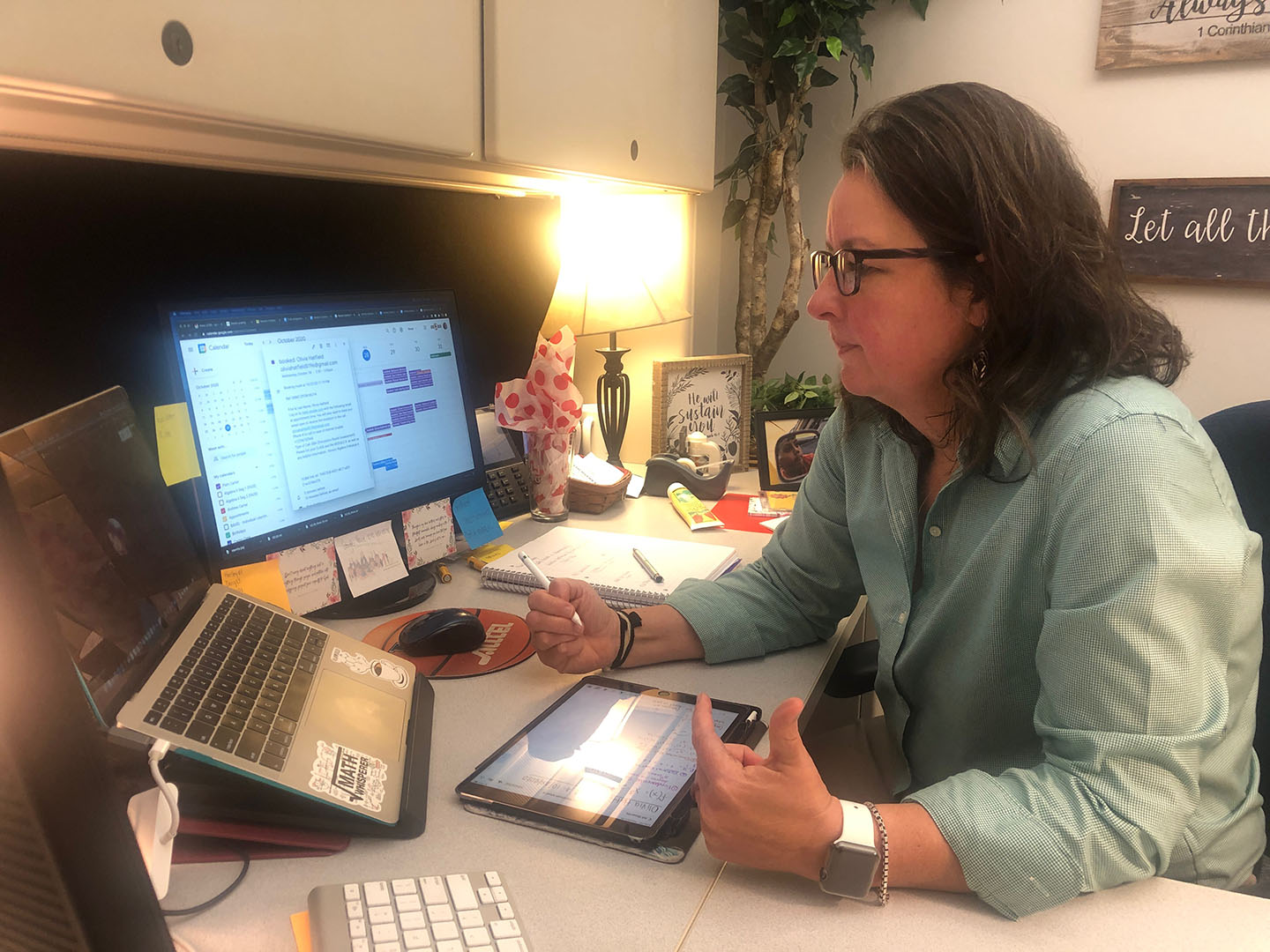 A woman sits at a desk with a computer in front of her, holding a virtual meeting.