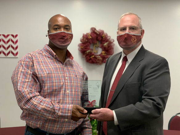 Two men in face masks stand next to each other holding onto a glass award.