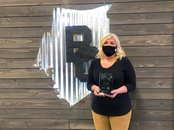 A woman wearing a face mask holds onto a glass award.