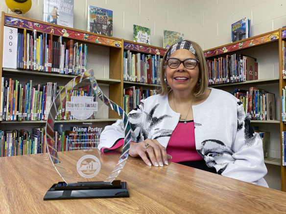 Picture of a smiling woman sitting at a table, a glass trophy sits in front of her.