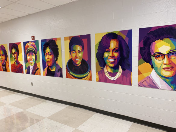 Brightly colored paintings of Black women hang on a wall in a school hallway.