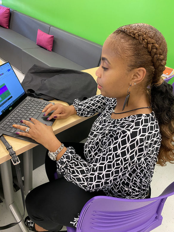 A woman sits at a computer in a brightly colored classroom.