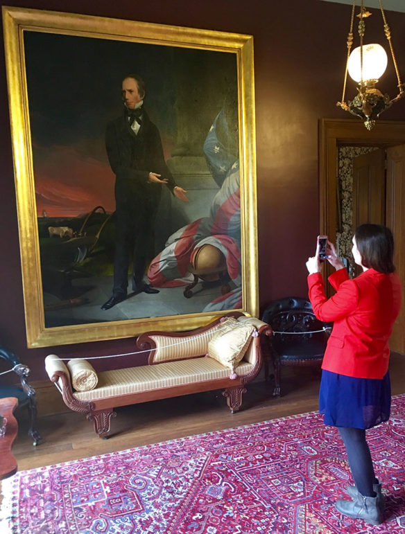 A woman takes a picture of a large painting leaning against a wall.
