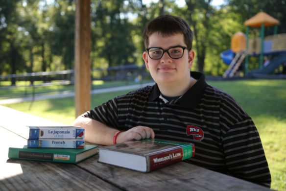 A young man sitting at a picnic table with books in front of him.