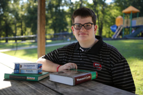 A young man sitting at a picnic table with books in front of him.