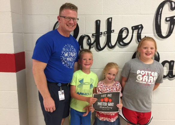 A picture of a smiling man standing in a school hallway with three young girls.