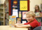 Picture of a young boy reading a book in a library.