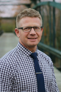 Picture of a man wearing glasses standing outside on a bridge.
