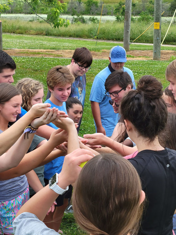 Picture of a group of smiling students standing outside in a large group with their hands linked together.