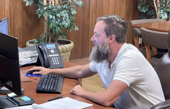 Picture of a man with a beard sitting in front of computers at a desk.