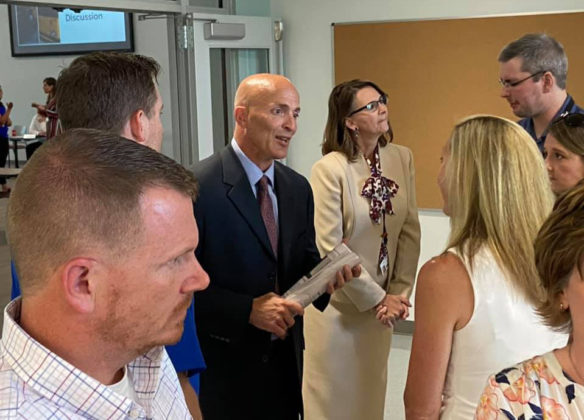 A man in a suit stands in the middle of a group of people while talking.