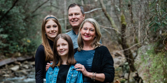 Picture of a man, two girls and one woman standing close together in the woods.