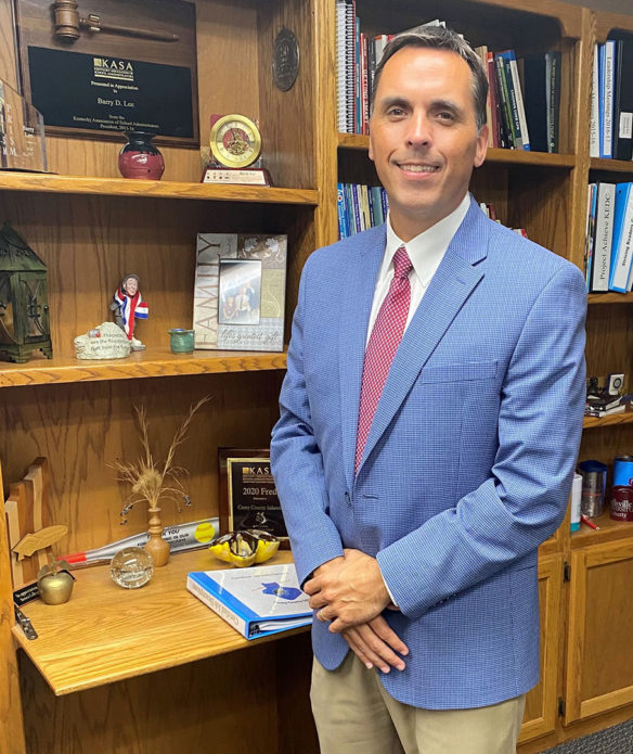 Picture of a man wearing a suit, standing in front of a cabinet.