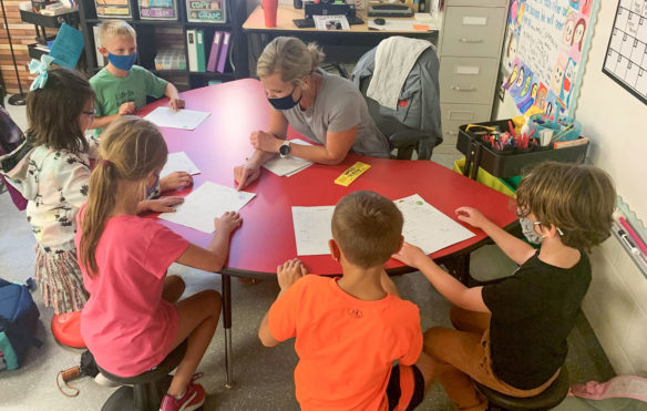 Picture of a woman working at a small table with five young children.